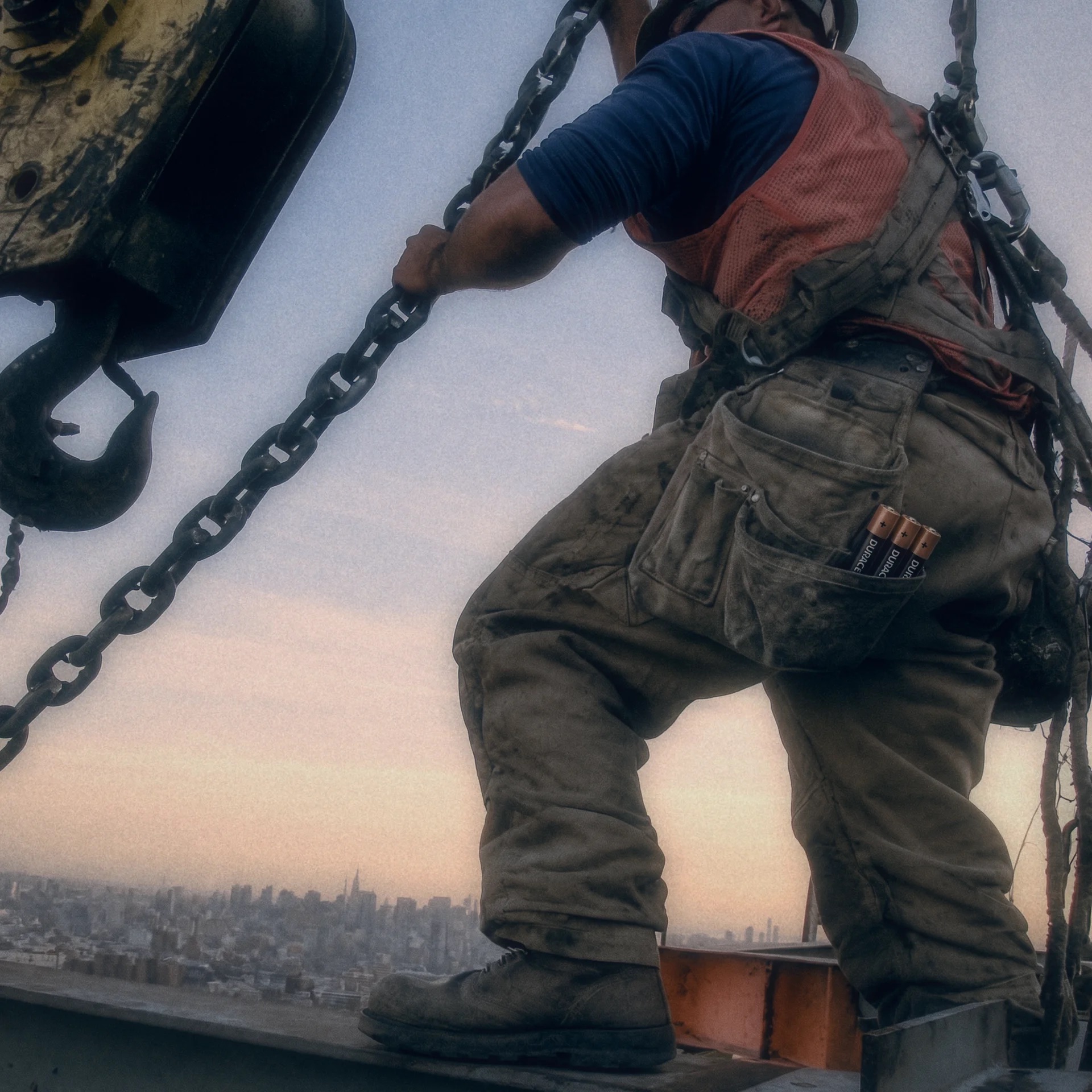 A steelworker climbing a chain high above a city, Duracell batteries in his pocket