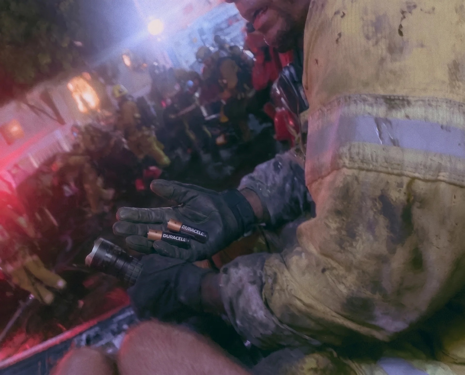 A firefighter's gloved hand holding two Duracell batteries and a flashlight