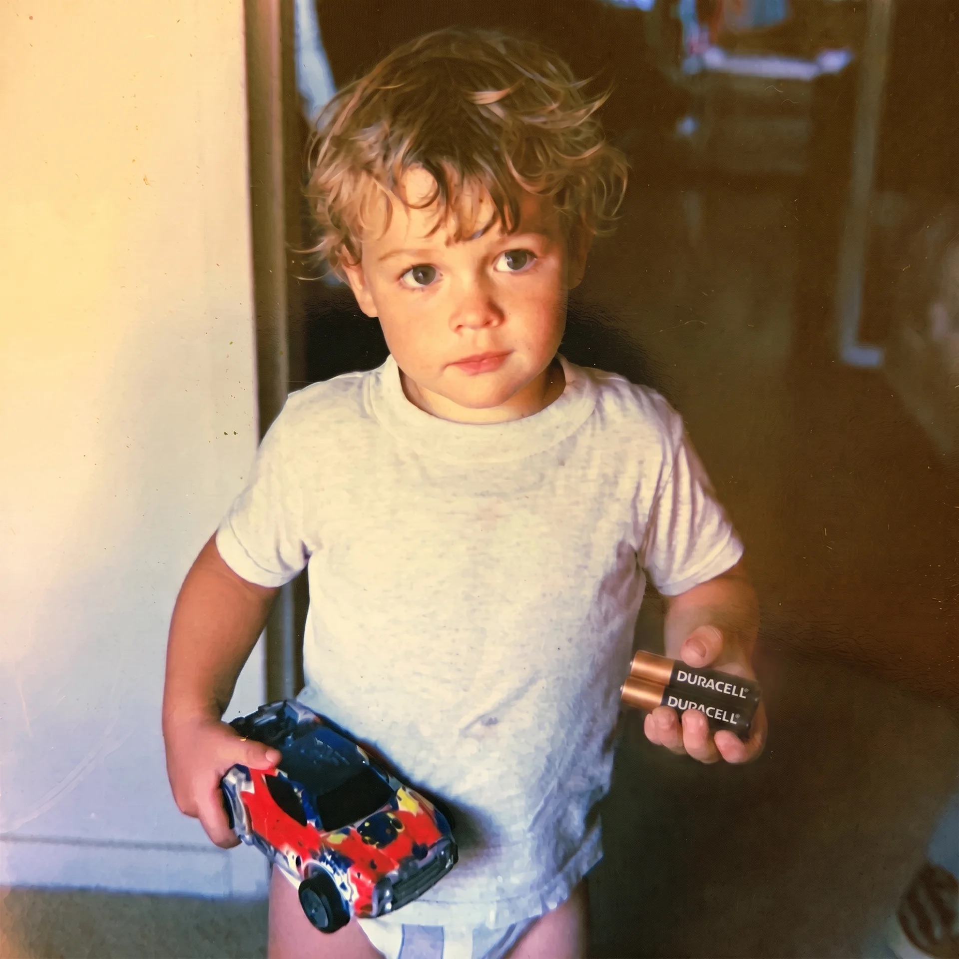 A toddler holding a toy car and a Duracell battery