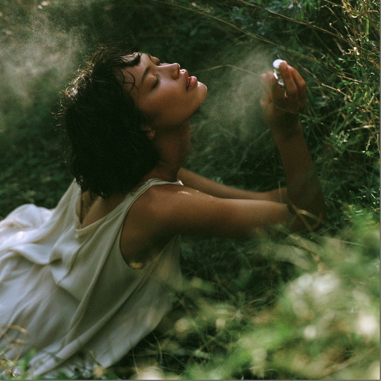 A woman reclining in the grass, misting fragrance over her face